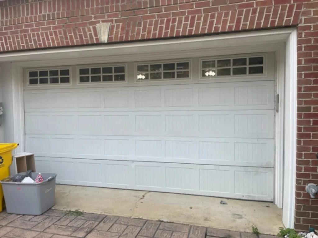White garage door with decorative windows on a red brick house and trash bins nearby.